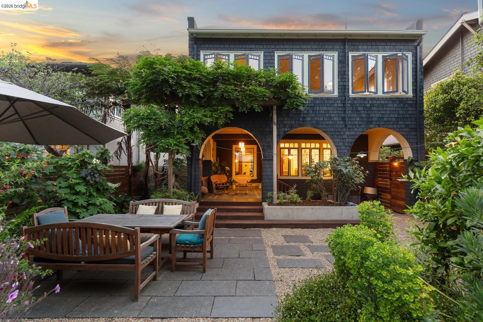 Dark shingle-sided house with arched patio openings overlooking a landscaped courtyard at sunset.