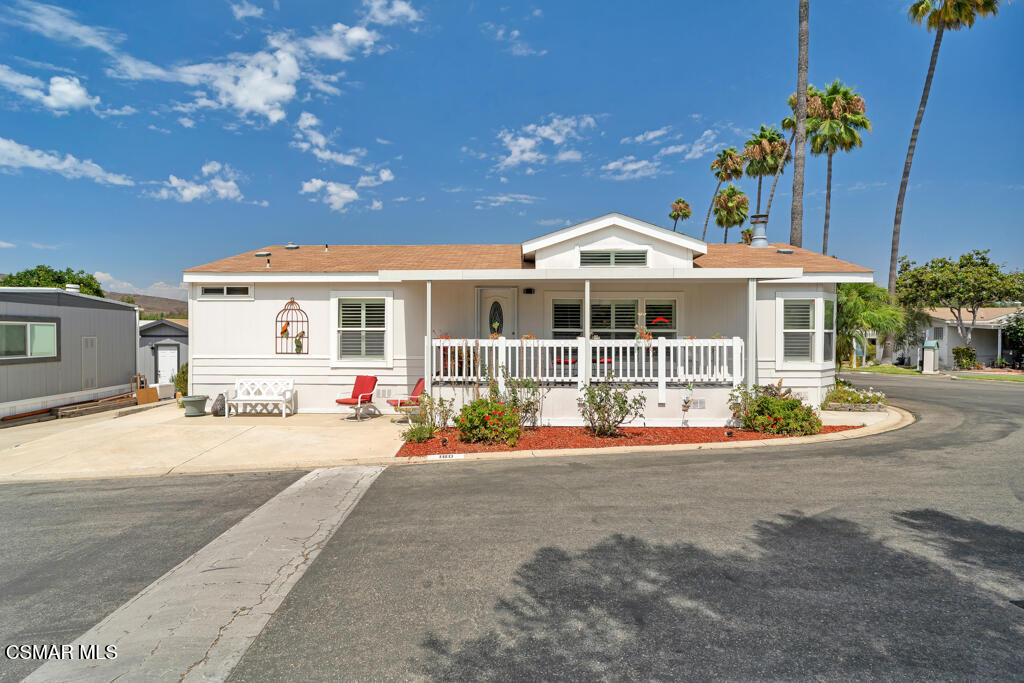White single-story home with a covered porch, front garden beds, and palm trees.