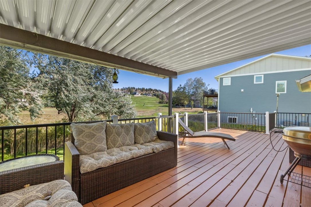 Covered deck with wicker seating and a grill overlooking a leafy yard and green space.