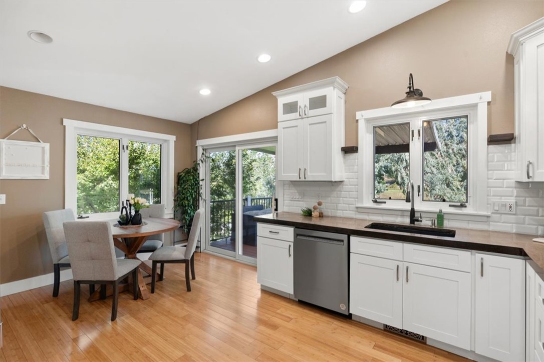 Kitchen with white cabinets and dark countertops, dining table, and windows overlooking greenery.