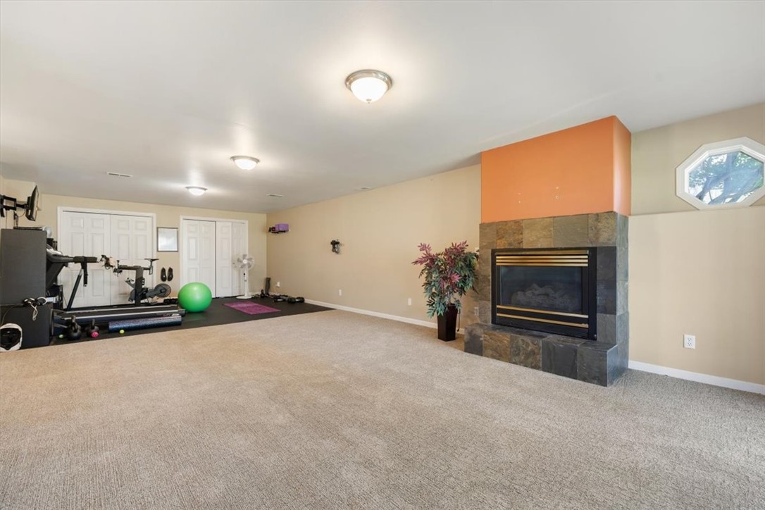 Carpeted recreation room with exercise equipment and a stone fireplace beneath an orange accent wall.