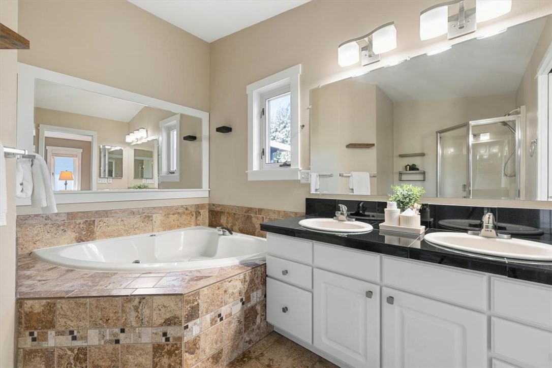 Bathroom with a tiled corner soaking tub, double-sink vanity, and glass-enclosed shower.