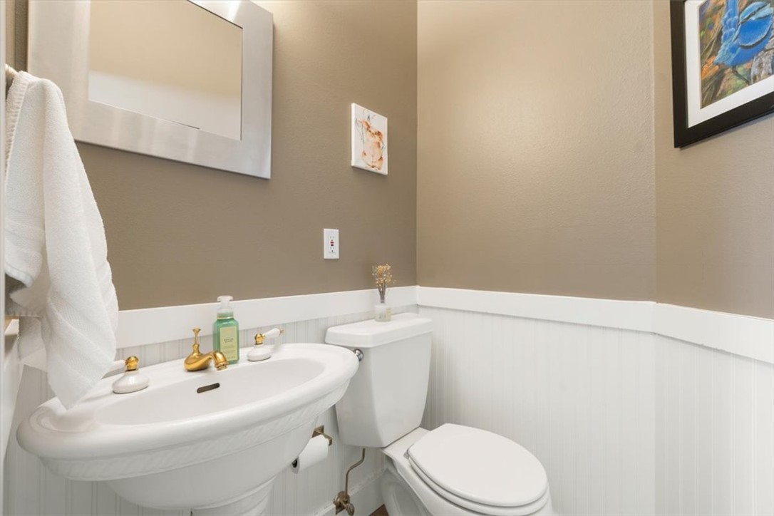Bathroom with a white pedestal sink and toilet, beadboard wainscoting, and framed art.