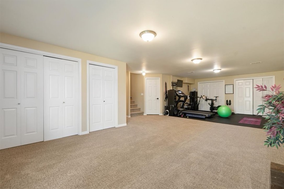 Carpeted exercise room with gym equipment, a green exercise ball, and multiple white closet doors.