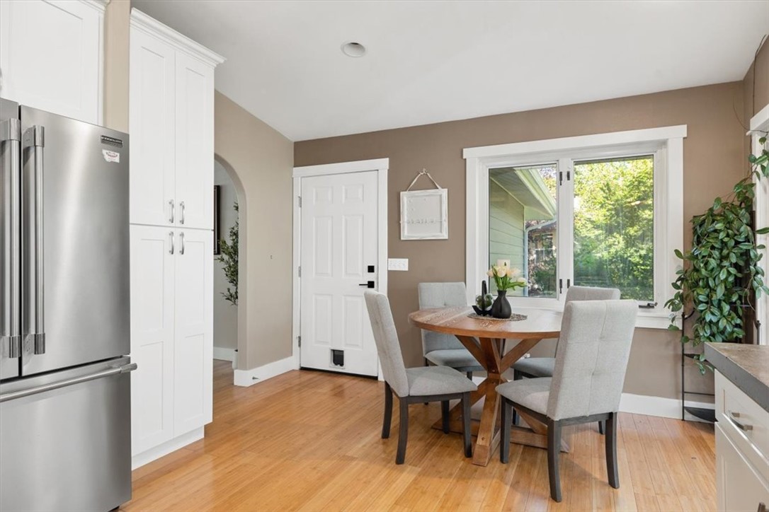 Kitchen dining area with a round wooden table, white cabinetry, and a large window.