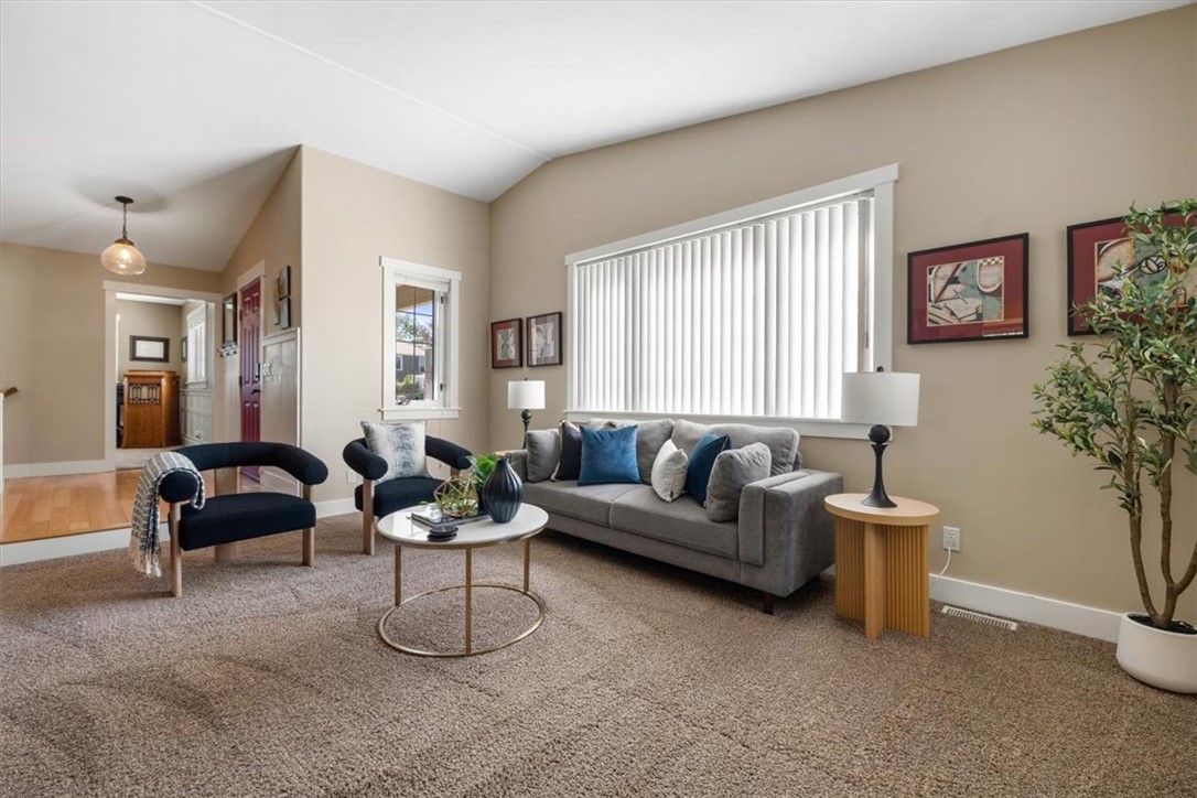 Living room with a gray sofa, dark armchairs, round coffee table, and large window with vertical blinds.
