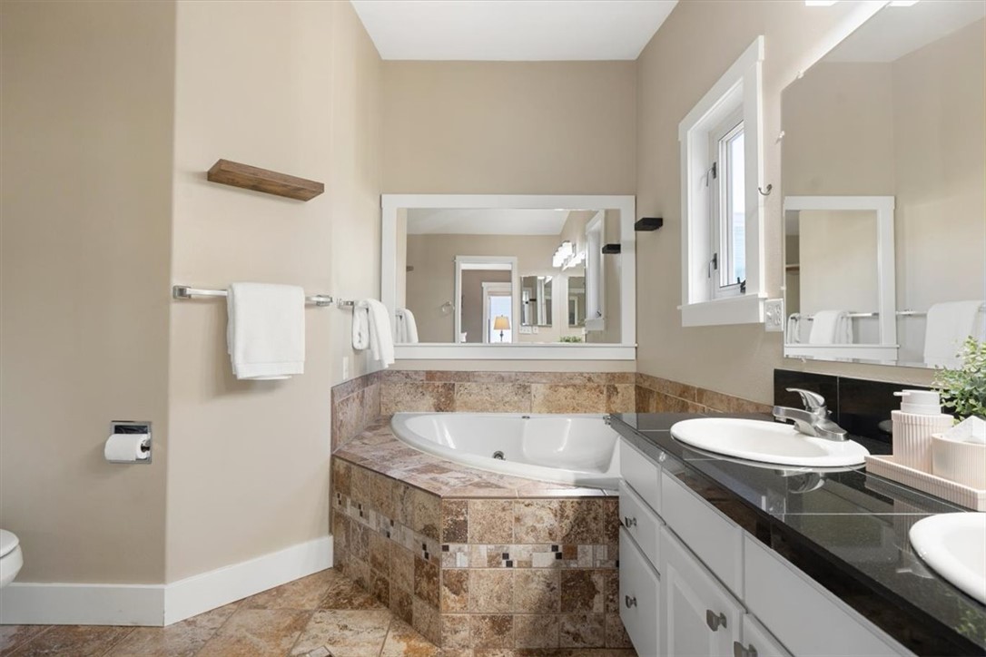 Bathroom with a corner soaking tub, stone-tile surround, and double vanity.