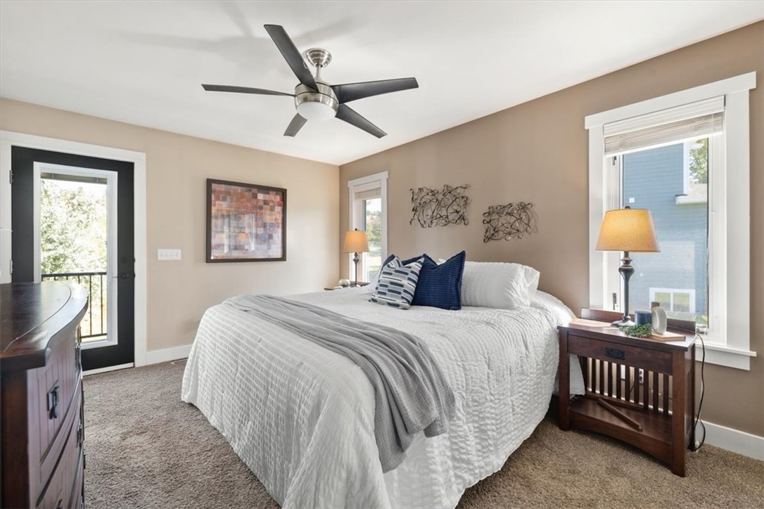 Staged bedroom with a white bed, gray throw, ceiling fan, and glass door to a balcony.