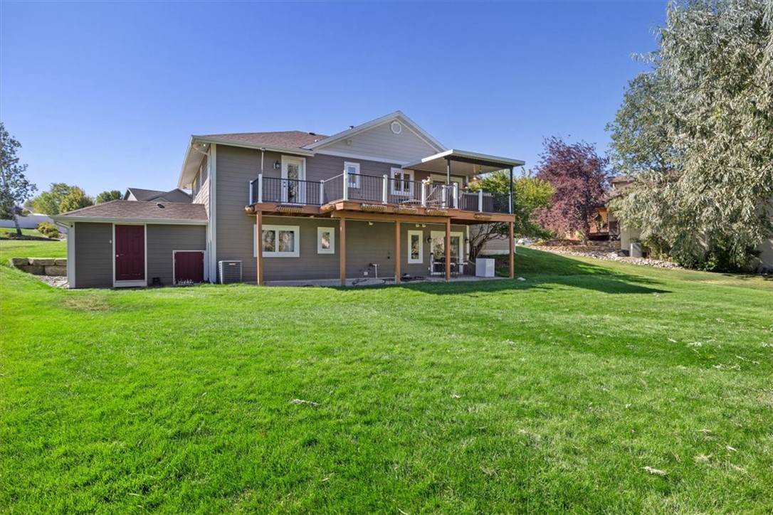 Rear of a gray two-story home with a raised deck, covered patio, and broad lawn.