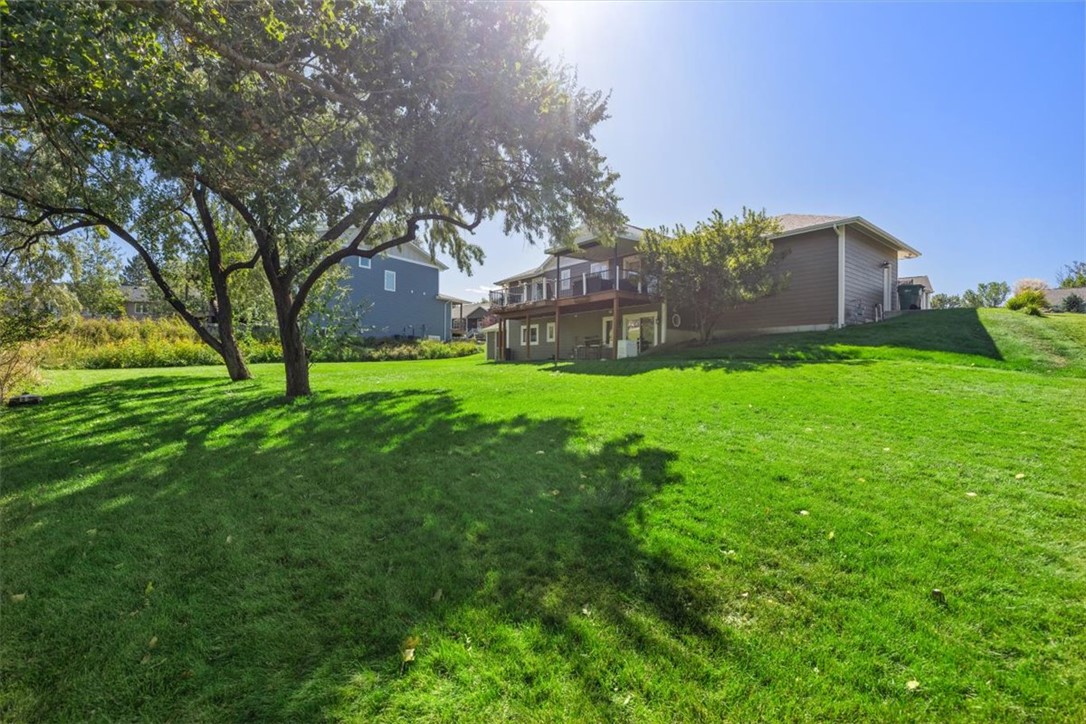 Rear of a two-story home with a raised deck, mature trees, and a broad green lawn.