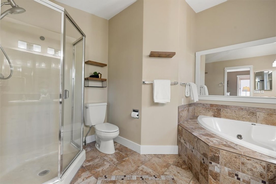 Bathroom with glass shower, built-in soaking tub, and patterned stone tile.
