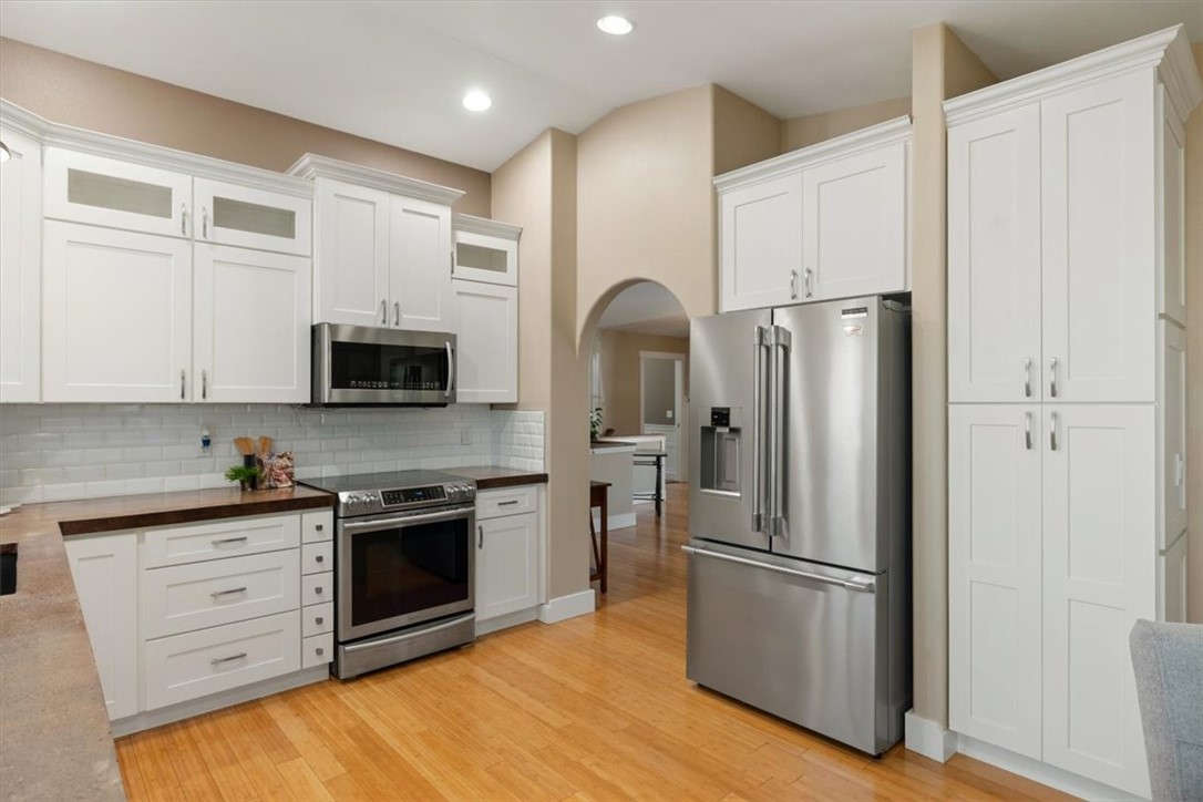 Kitchen with white cabinetry, stainless steel appliances, subway tile backsplash, and warm wood floors.