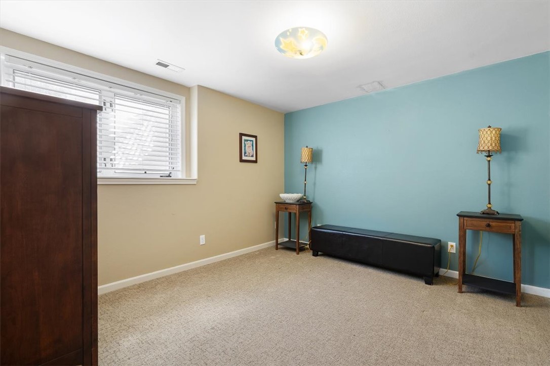 Carpeted room with a turquoise accent wall, dark bench, side tables, and a window with blinds.