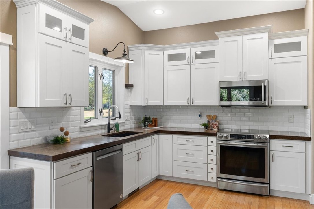Kitchen with white cabinets, dark countertops, stainless steel appliances, and hardwood floors.