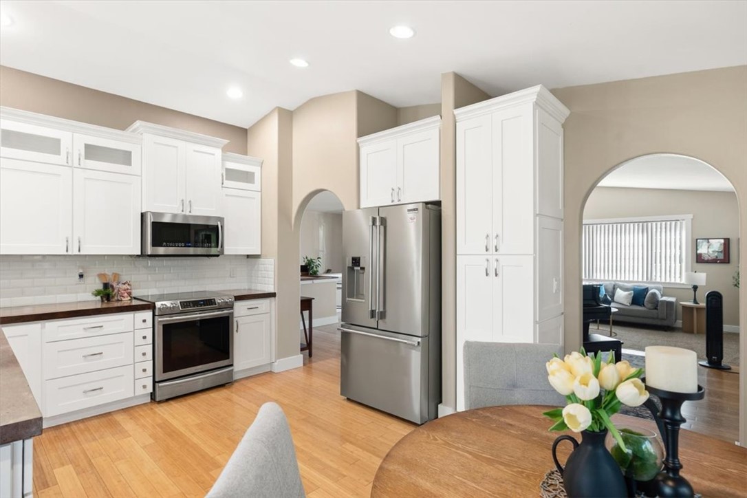 Kitchen with white cabinets, stainless steel appliances, hardwood floors, and an arched opening to the living room.