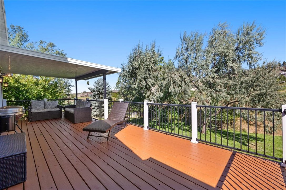 Spacious deck with black railings, a covered seating area, and a chaise overlooking mature trees.