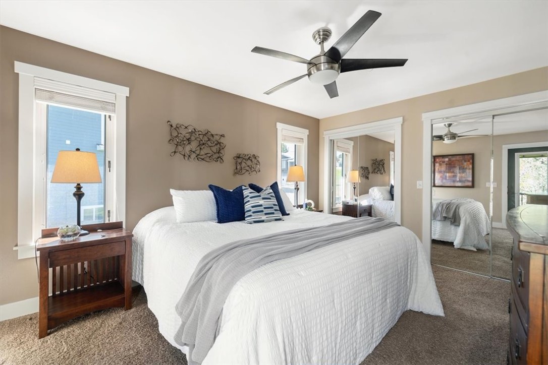 Primary bedroom with a white bed, blue pillows, ceiling fan, and mirrored closet doors.
