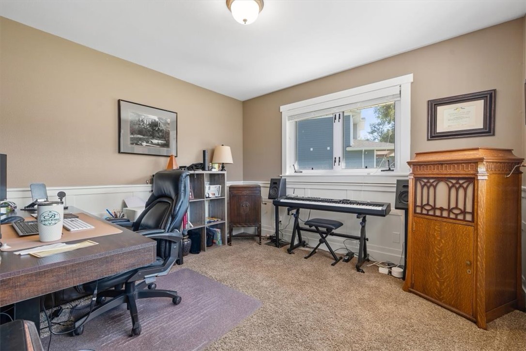 Home office with a desk, computer, keyboard beneath a window, and tall wooden cabinet.