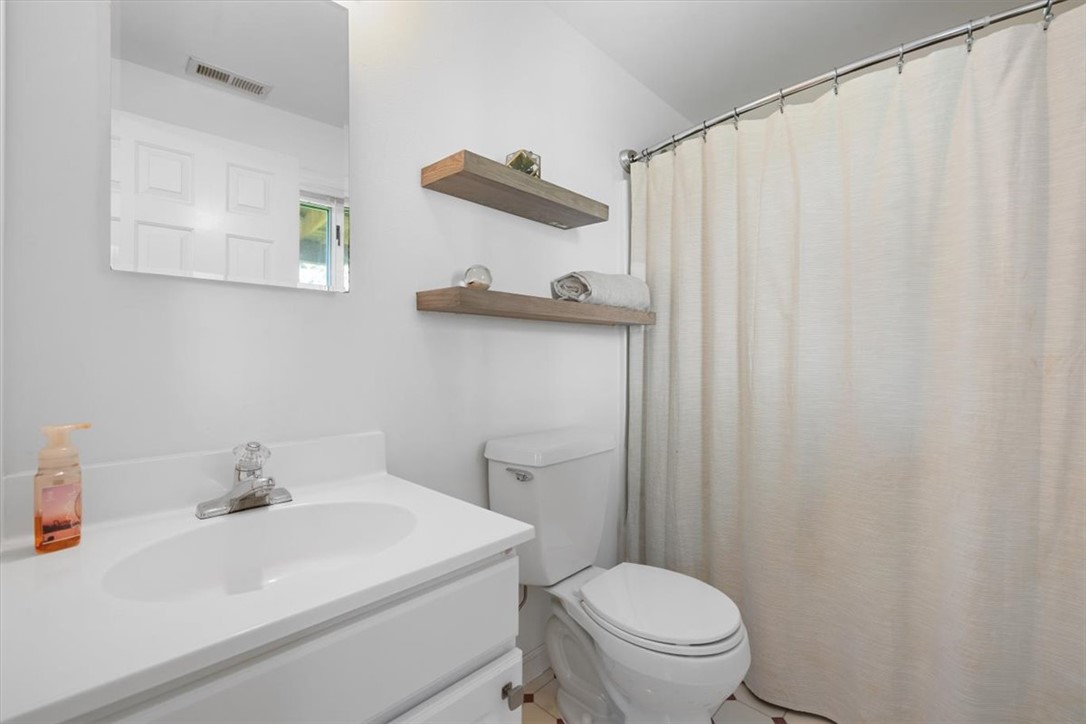 Bathroom with a white vanity, toilet, beige shower curtain, and wooden floating shelves.