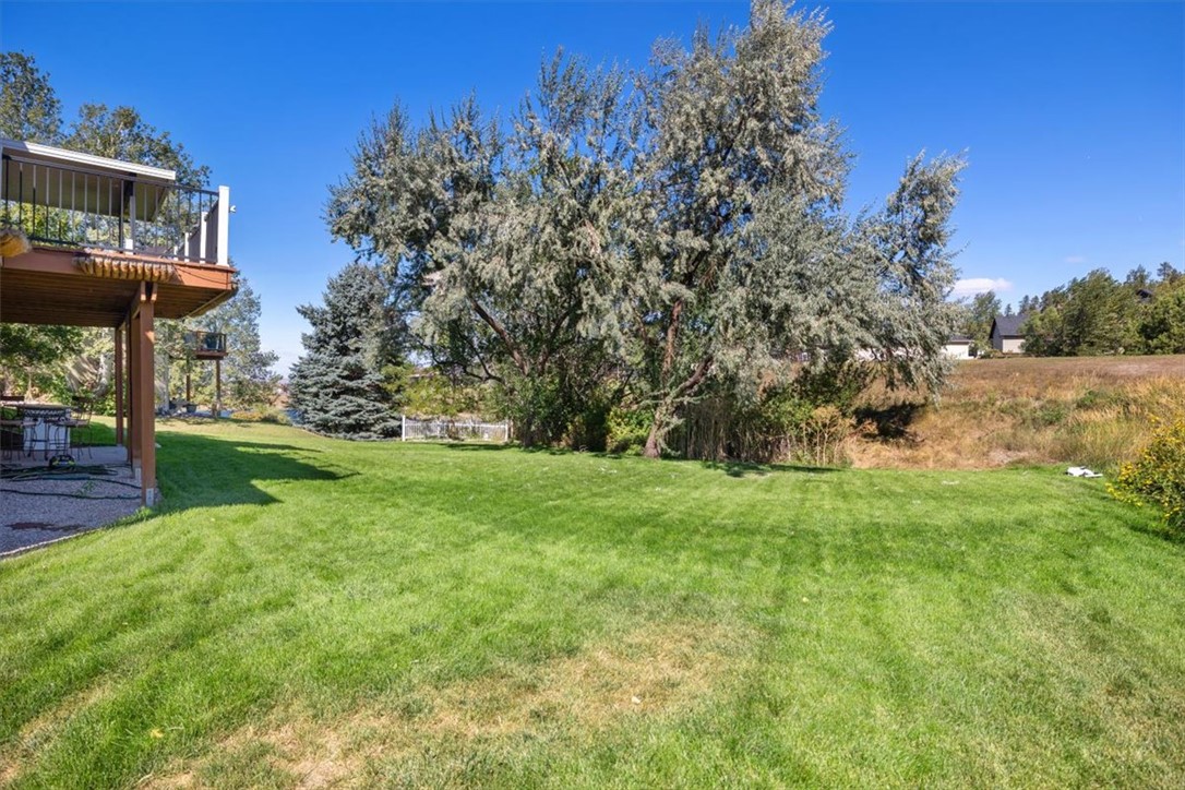 Backyard with a broad lawn, mature trees and a raised deck with outdoor seating.