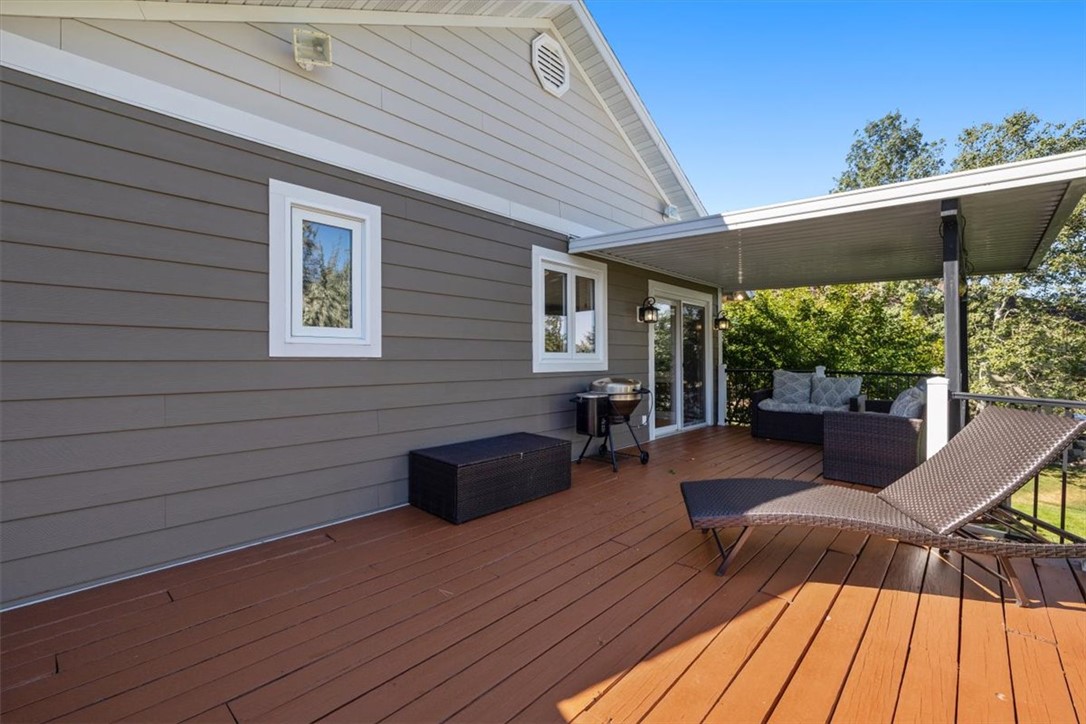 Raised wooden deck with covered seating area, chaise lounge, grill, and gray house siding.