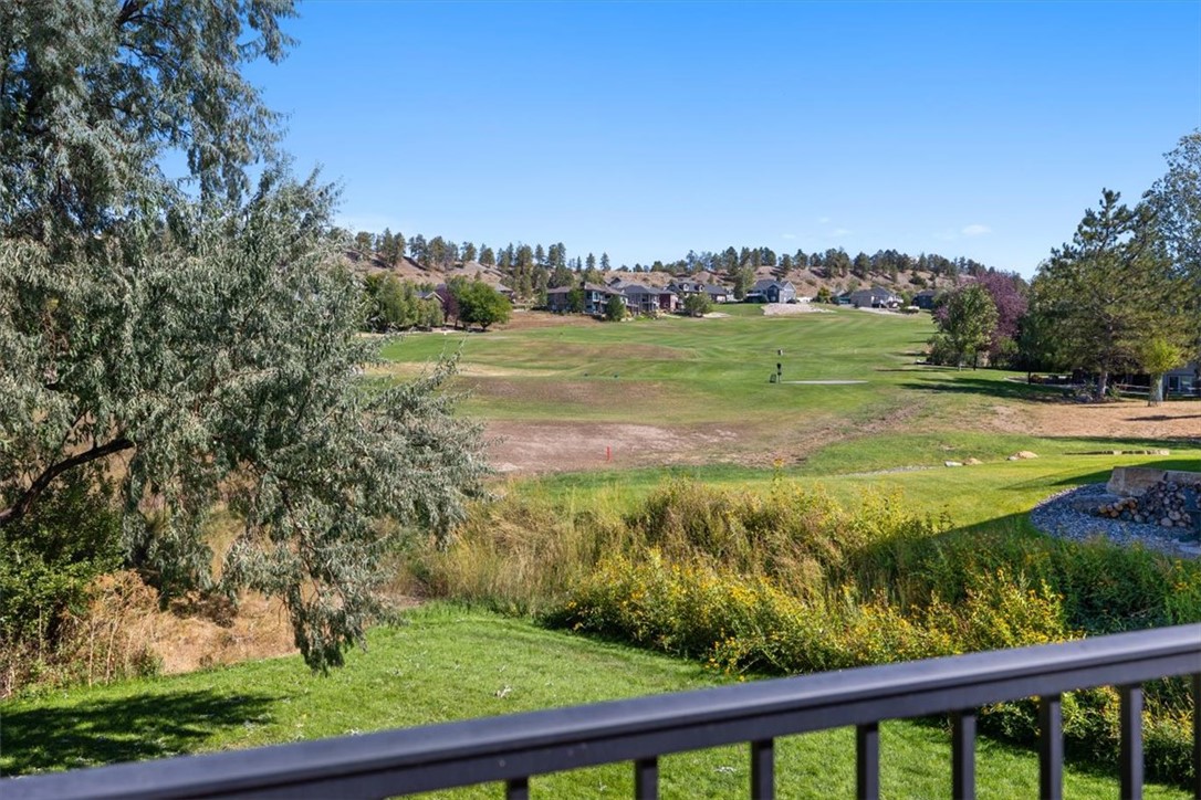 Golf course and fairway viewed from a deck, framed by trees and distant homes.