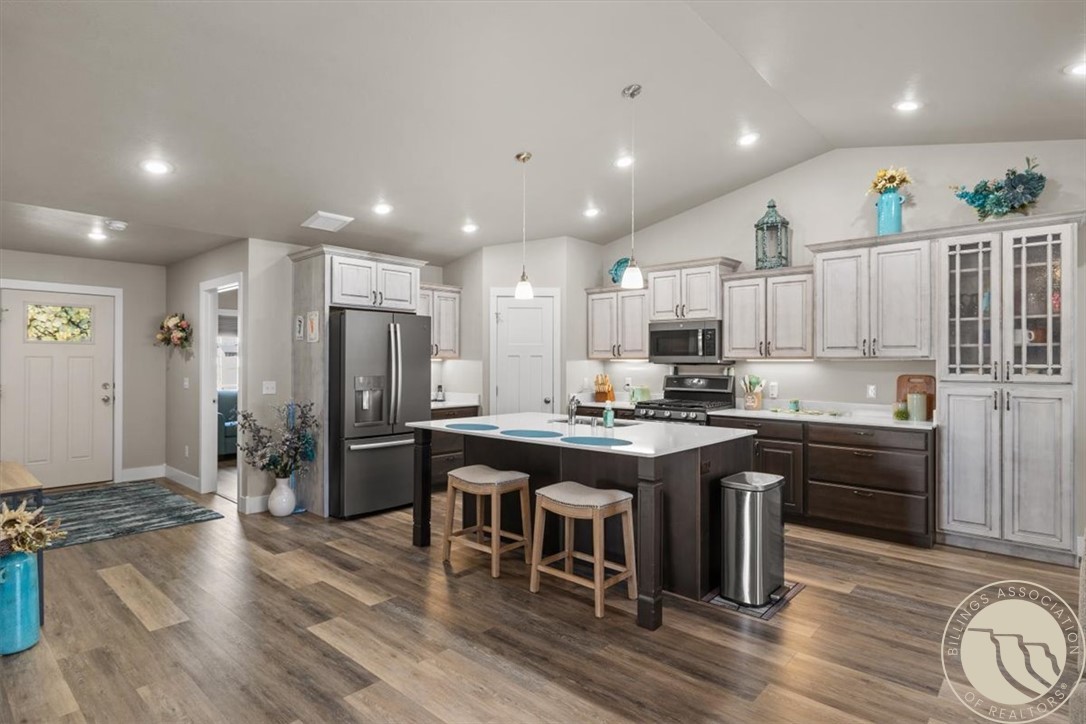 Kitchen with a large island, stainless steel appliances, white cabinetry, and wood-look flooring.