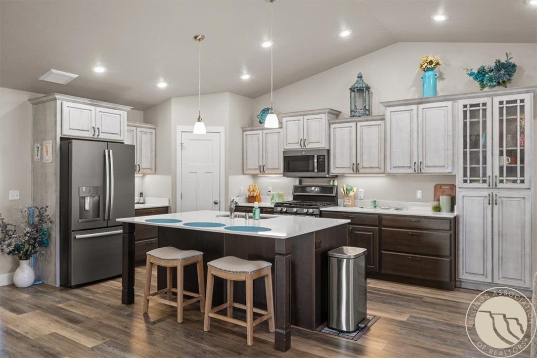 Kitchen with a large island, bar stools, white cabinets, and stainless steel appliances.
