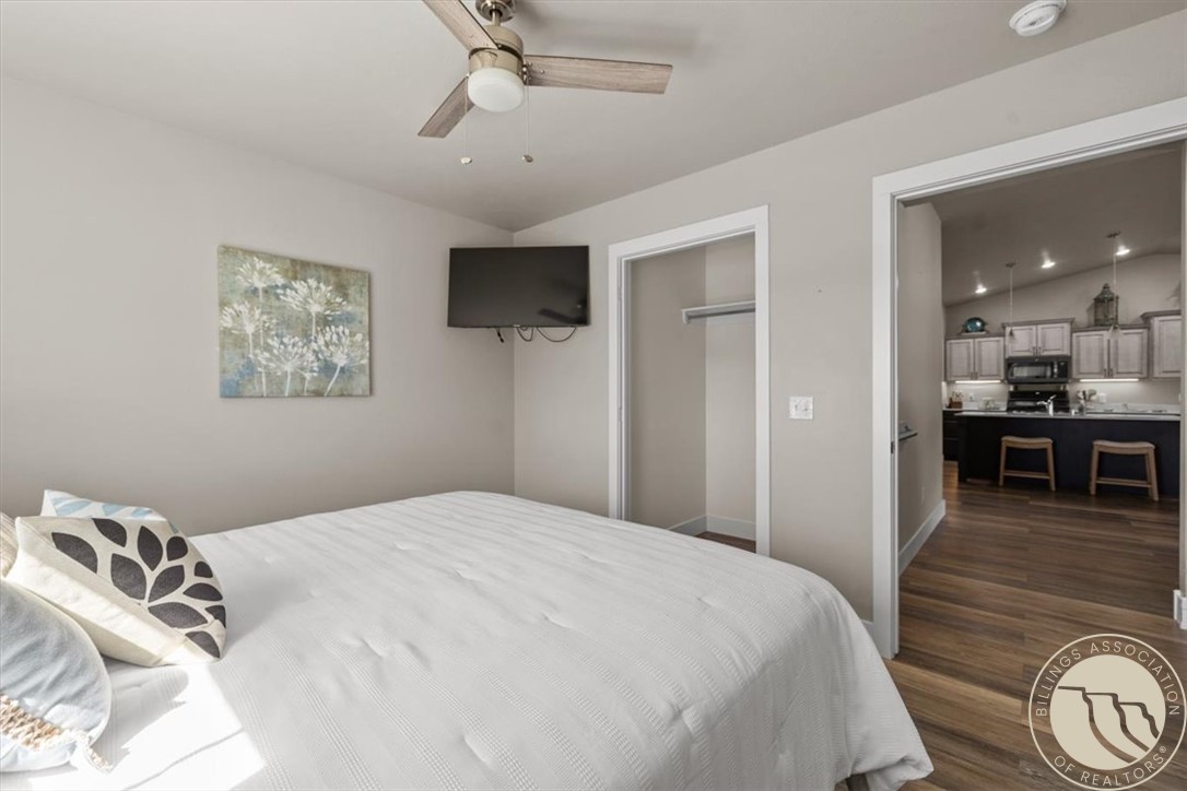 Bedroom with a white-covered bed, wall-mounted TV, open closet, and view into the kitchen.
