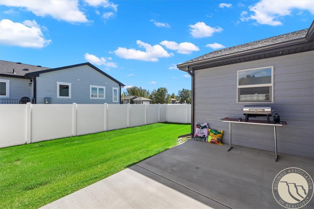Backyard patio with a grill beside a fenced green lawn.
