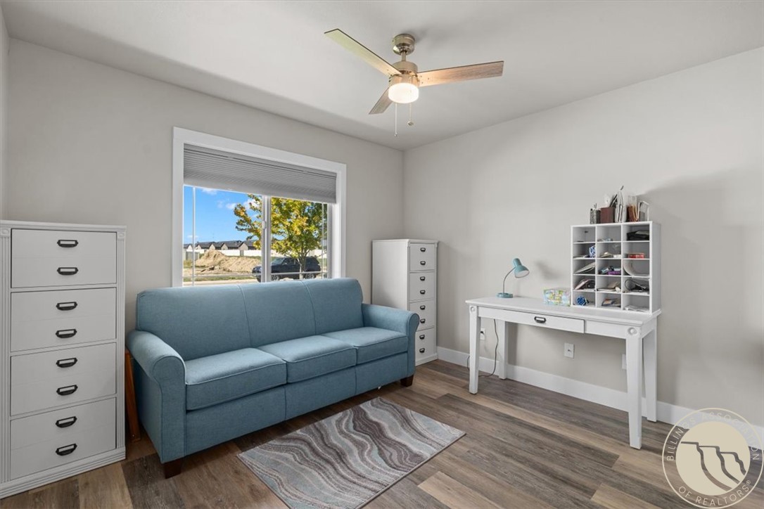 Furnished home office with a blue sofa, white desk, cubby shelving, and wood-look flooring.