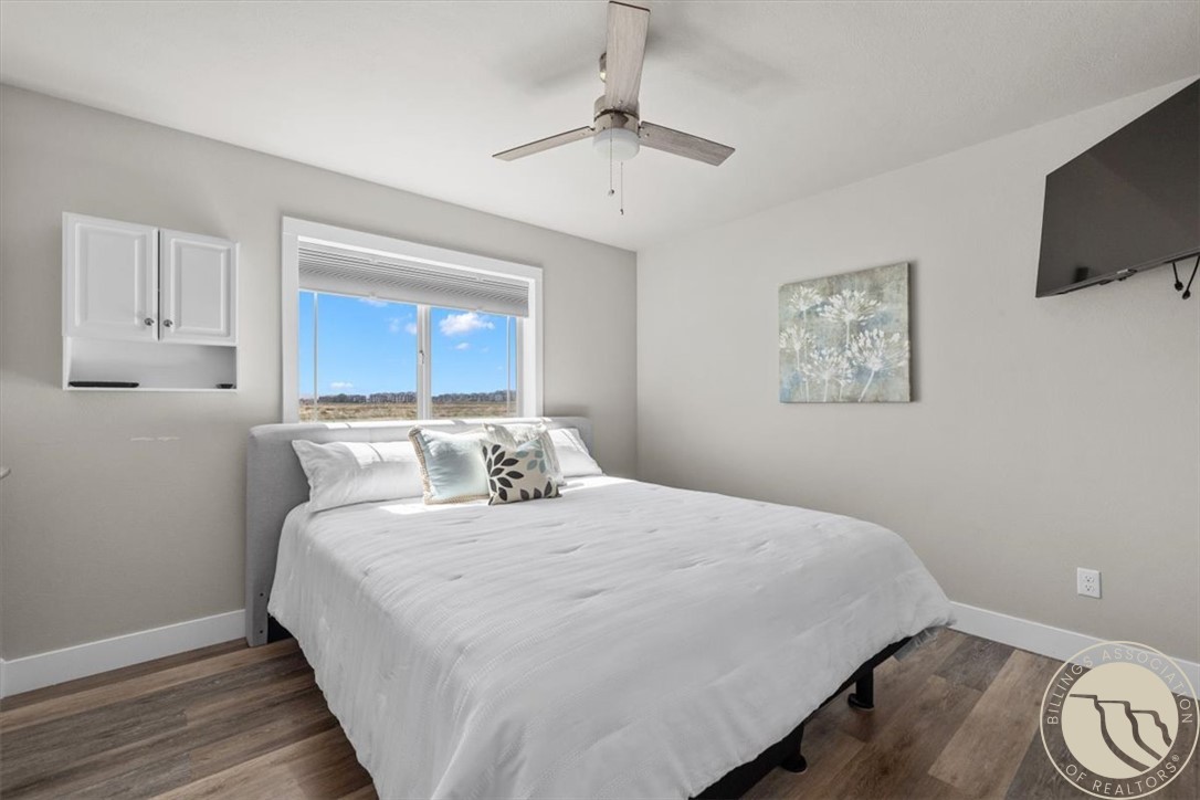 Furnished bedroom with a large bed, ceiling fan, and window overlooking open land.
