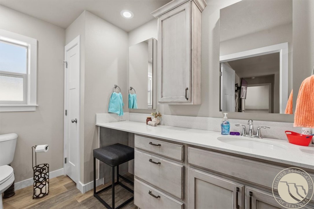 Bathroom with a long double-sink vanity, pale gray cabinets, large mirror, and wood-look flooring.