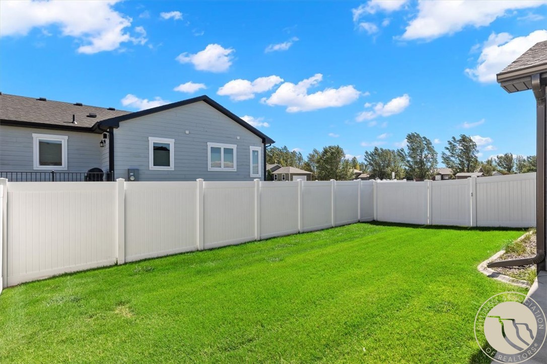Fenced backyard with a bright green lawn and gray-sided house beyond the fence.