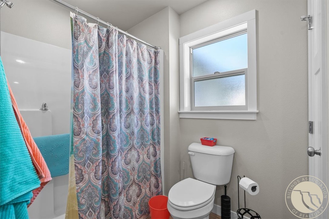 Bathroom with a paisley shower curtain, white toilet, and frosted window.
