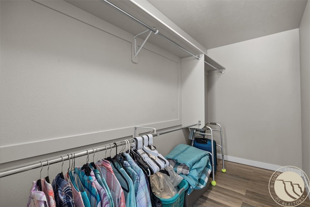 Walk-in closet with clothes on hangers, upper shelves, and laundry baskets.
