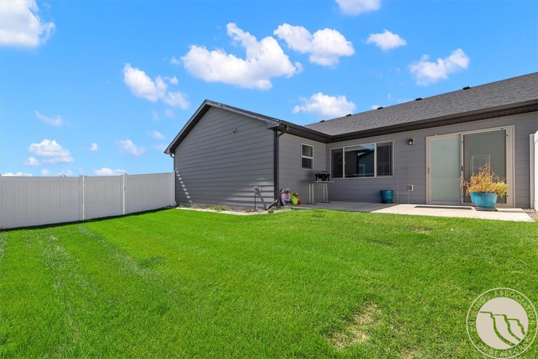 Fenced backyard with a broad green lawn and gray house with sliding glass patio doors.