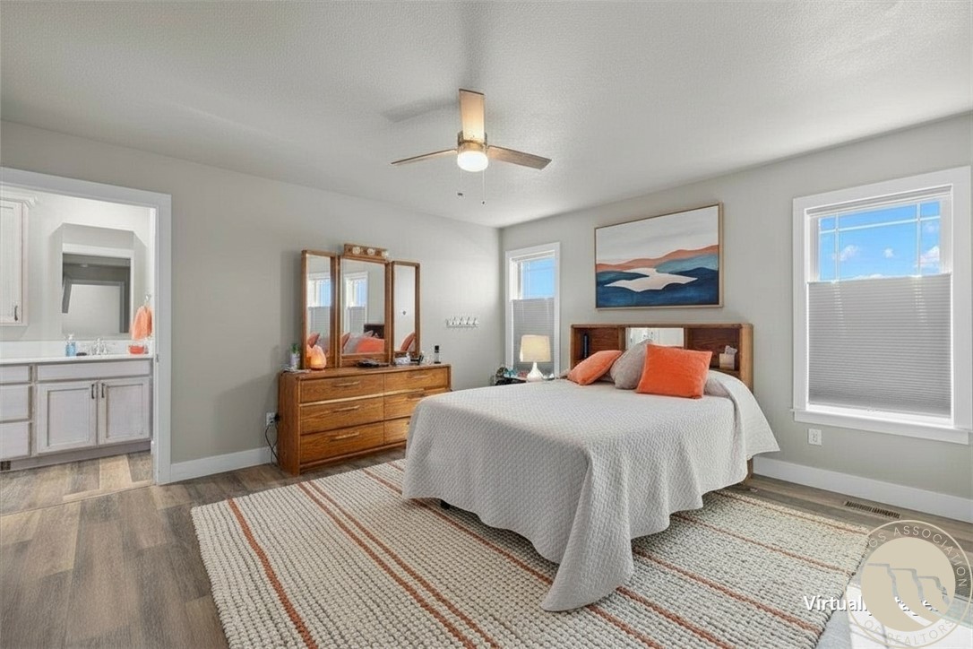 Staged bedroom with a white bed, rust-colored pillows, mirrored dresser, and striped rug.