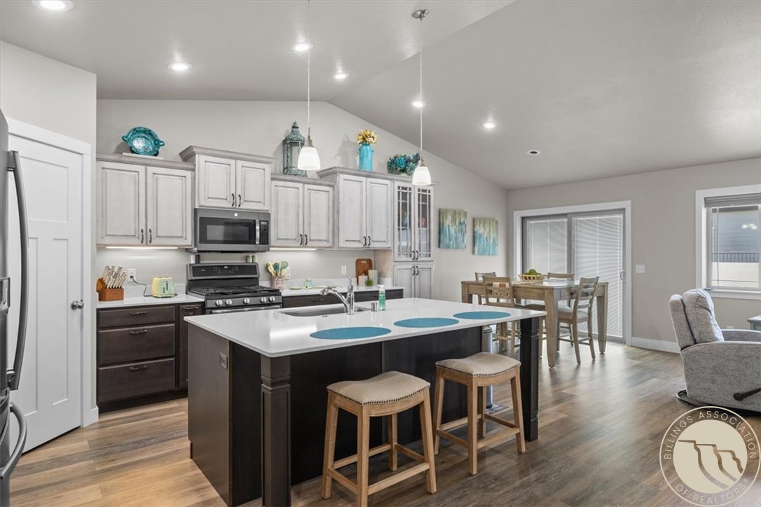 Kitchen with a large dark island, white cabinetry, stainless steel appliances, and an adjoining dining area.