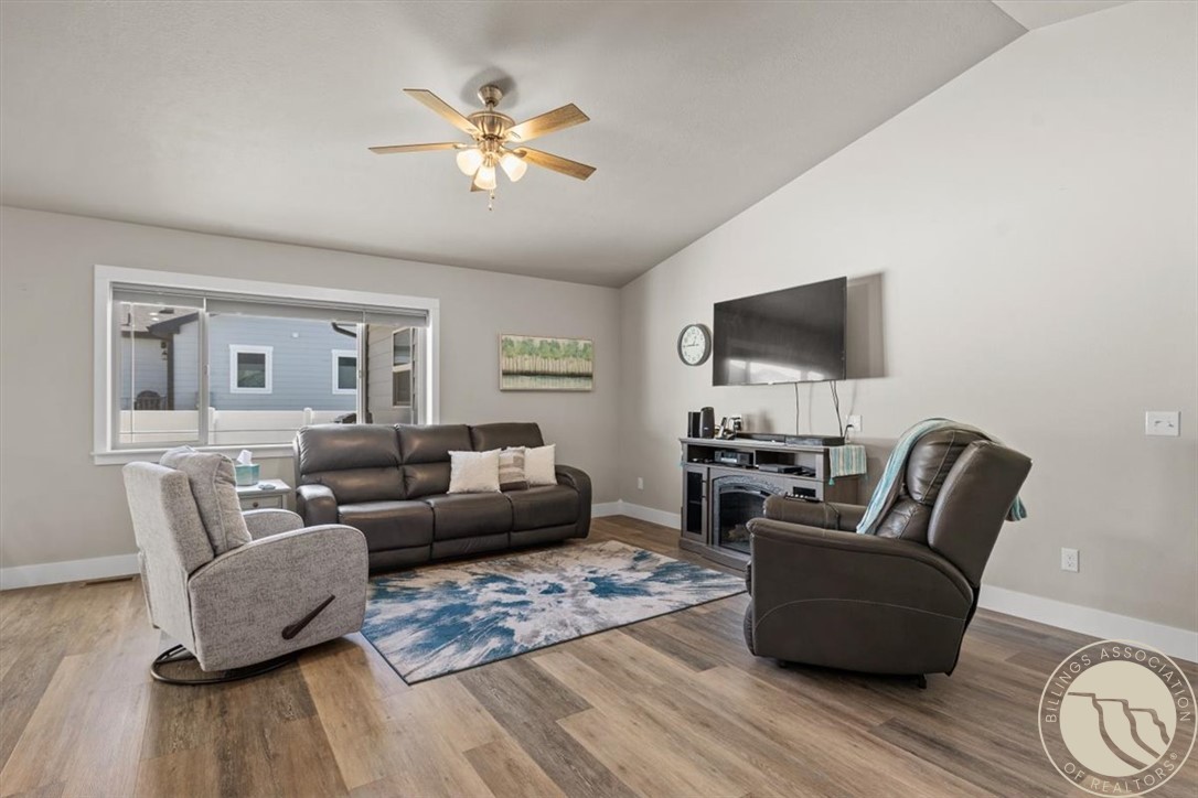 Living room with leather seating, a blue patterned rug, wall-mounted television, and ceiling fan.