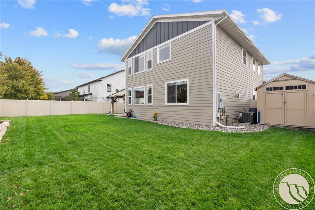 Two-story beige home and storage shed beyond a broad, fenced green lawn.