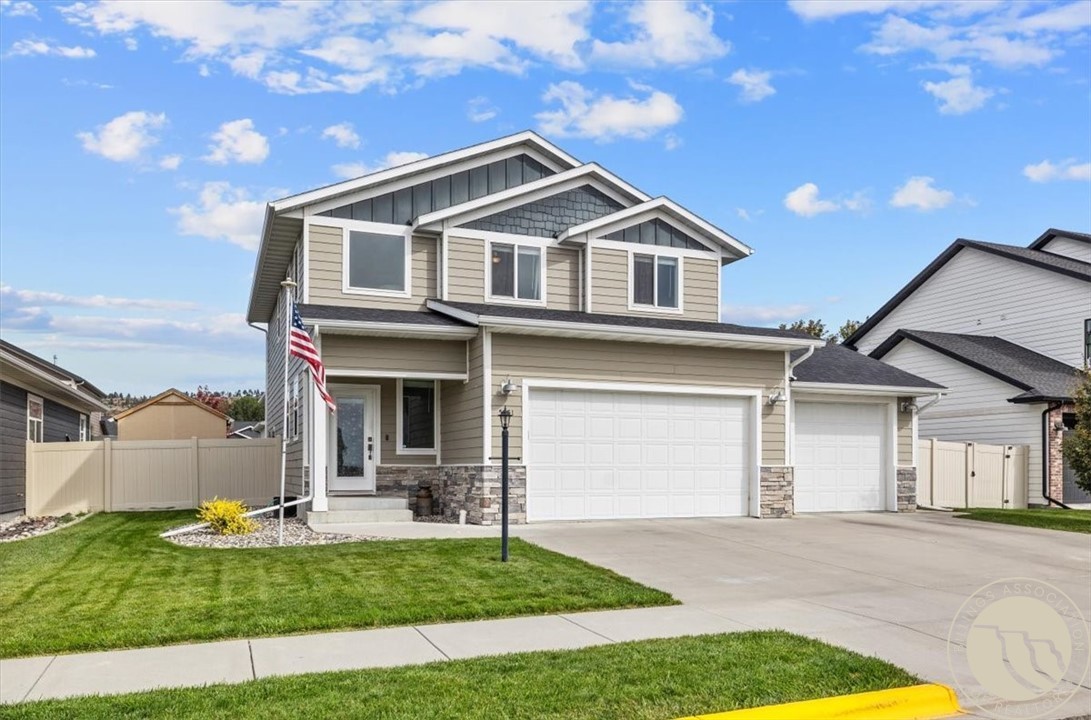Two-story beige home with stone accents, three-car garage, front lawn, and an American flag.
