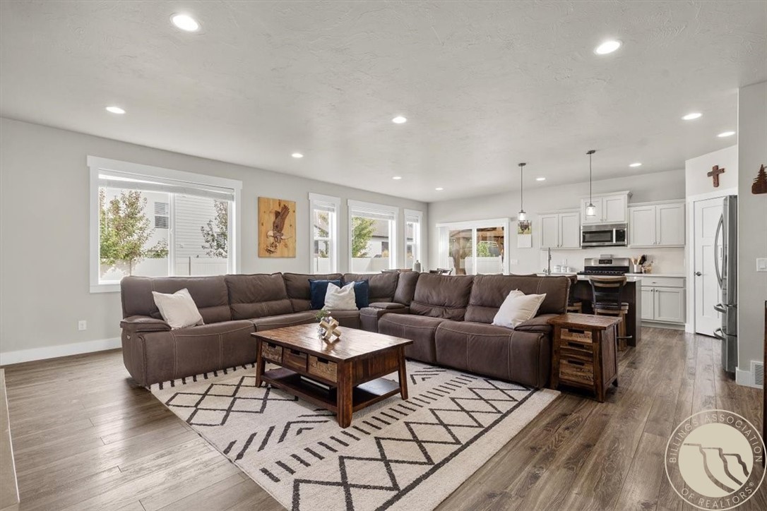 Open living room with a large sectional, patterned rug, and adjoining white kitchen.