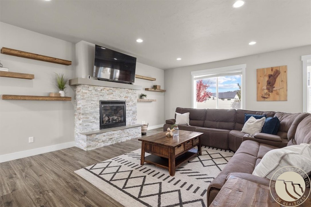 Living room with a stone fireplace, wall-mounted television, and brown sectional sofa.