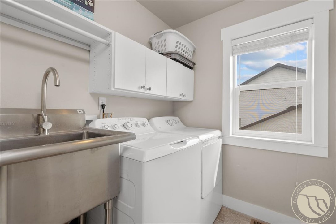 Laundry room with a stainless utility sink, washer and dryer, overhead cabinets, and a window.