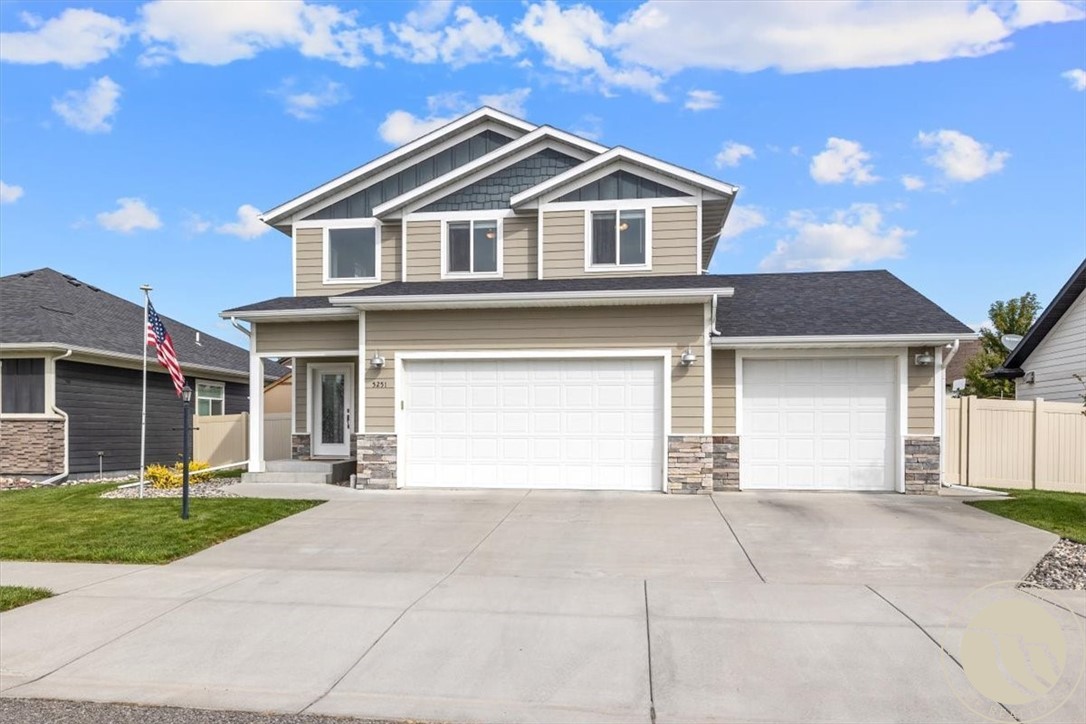 Two-story beige house with stone accents, two white garage doors, and a wide concrete driveway.