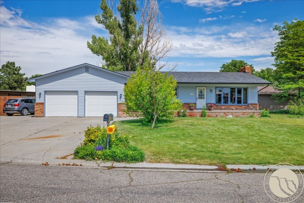 Single-story blue house with a two-car garage, brick accents, and a broad green lawn.