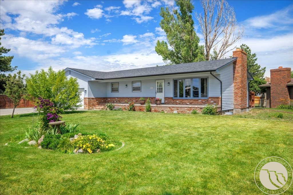 Single-story ranch home with a brick chimney, broad green lawn, and flower garden.