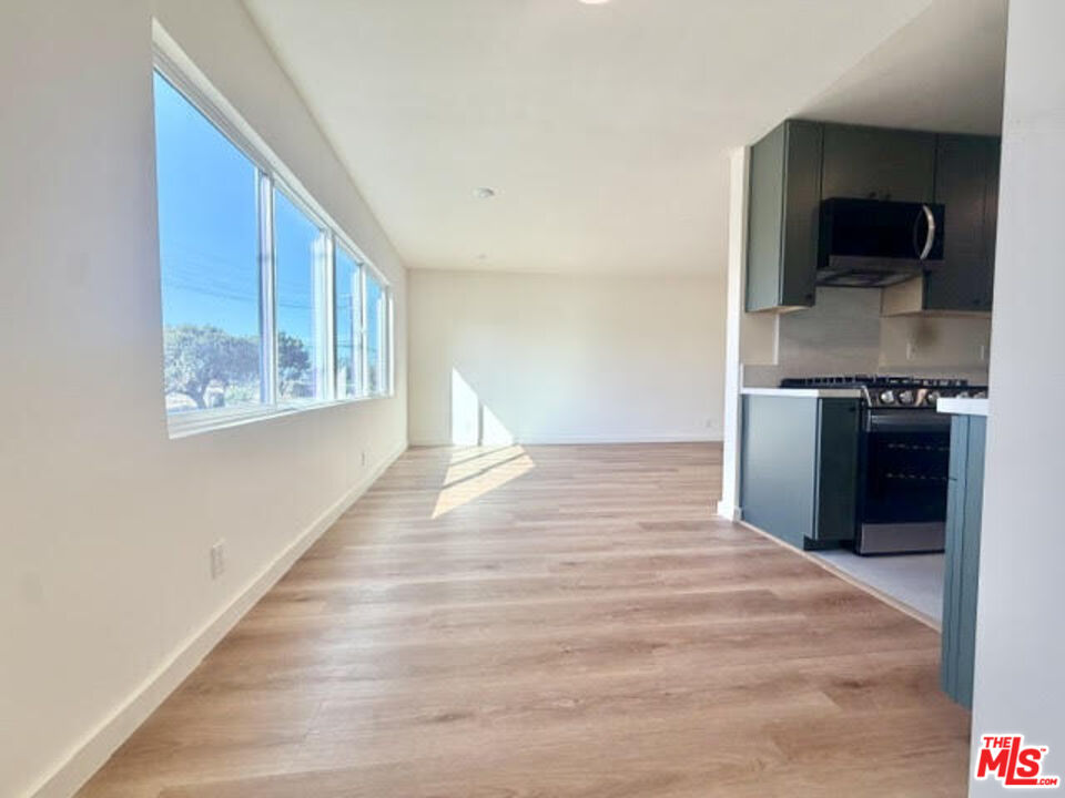 Vacant open-plan living area with wood floors, large windows, and a modern kitchen.
