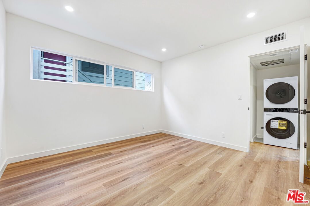 Empty room with light wood floors, high windows, and a stacked washer and dryer in the adjoining closet.